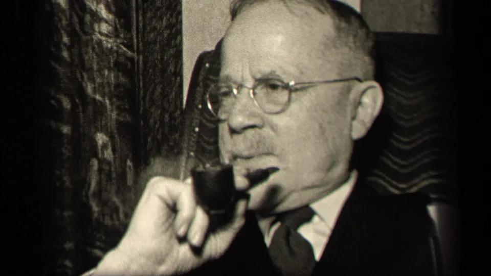 In the 1942 Sebring, Ohio home-movie frame, the seated man turns in profile with a pipe, suit, tie, and round eyeglasses visible.