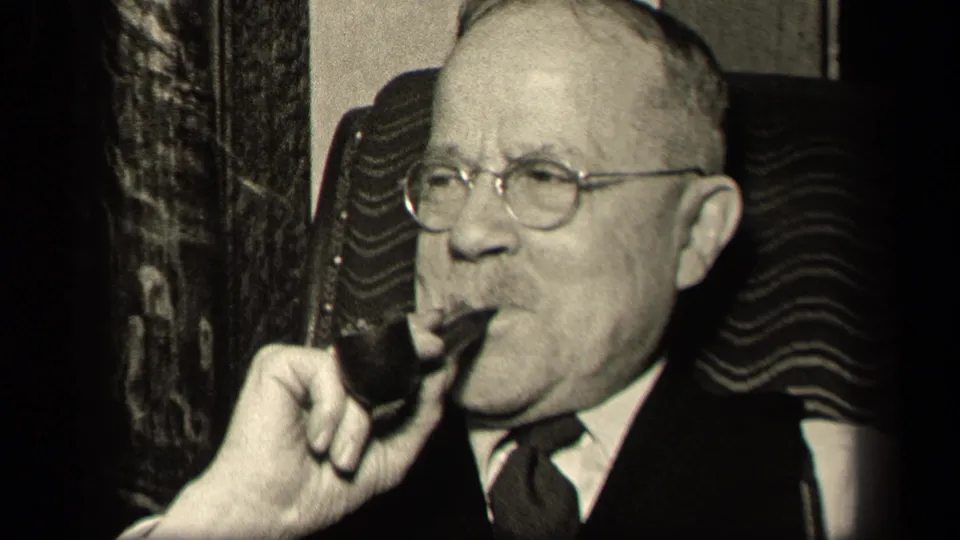 In this 1942 Sebring, Ohio frame, the older suited man holds a pipe in his mouth while seated against a patterned chair back.