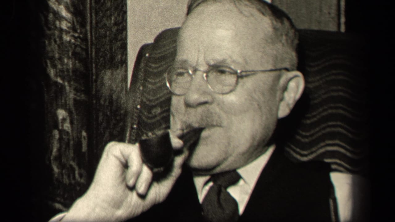 In a 1942 Sebring, Ohio home-movie frame, an older man in a dark suit and round glasses sits in a patterned armchair while holding a smoking pipe near his mouth.