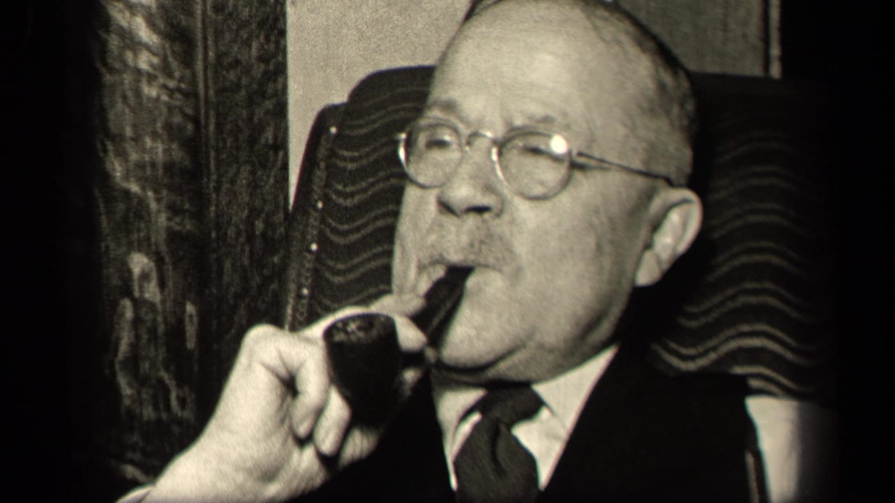 Older man in glasses holding a smoking pipe to his mouth while seated indoors.