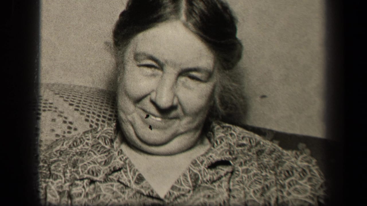 In the 1942 Sebring, Ohio home-movie frame, an elderly woman in a patterned blouse smiles toward the camera while seated against an upholstered back and plain wall.
