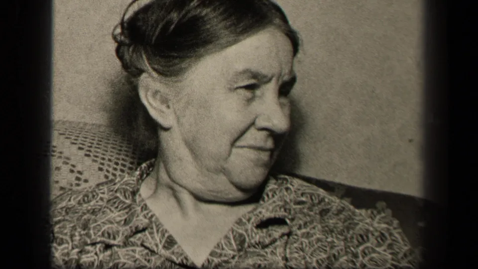 The 1942 Sebring, Ohio home-movie frame shows the elderly woman in side profile, seated close to the camera with a patterned blouse and upholstered background.