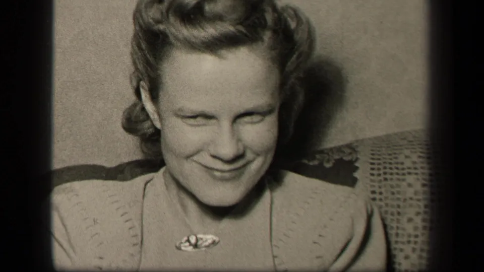 Younger woman wearing a brooch and light sweater smiles in the Sebring, Ohio home setting recorded on 8mm film.