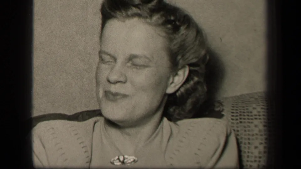 Younger woman in a light sweater reacts mid-conversation, eyes closed and head turned, in the 1942 home-movie frame.