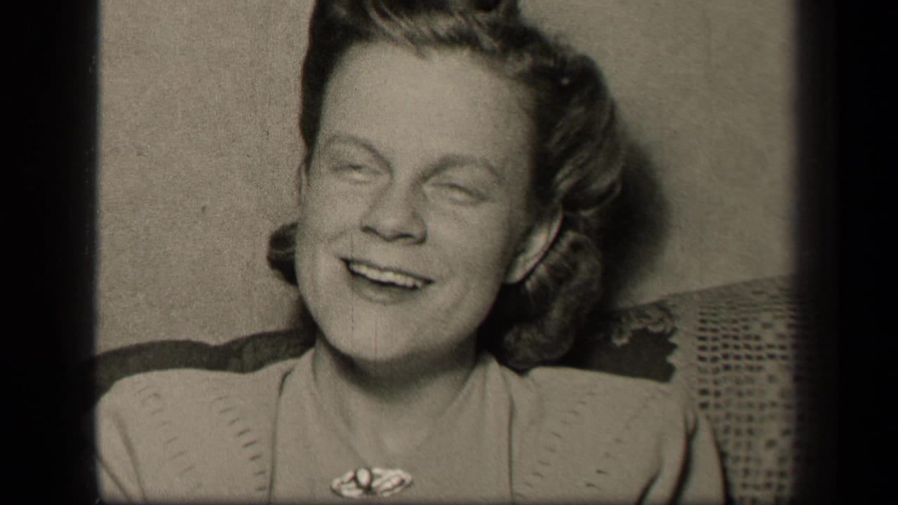 In this 1942 Sebring, Ohio home-movie frame, a young woman in a light dress and brooch smiles while seated on patterned upholstery.