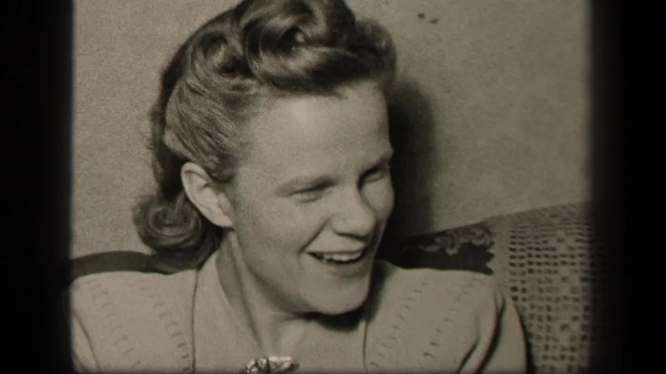 A candid 1942 home-movie frame shows the seated woman laughing and lowering her gaze in a private Sebring, Ohio interior.