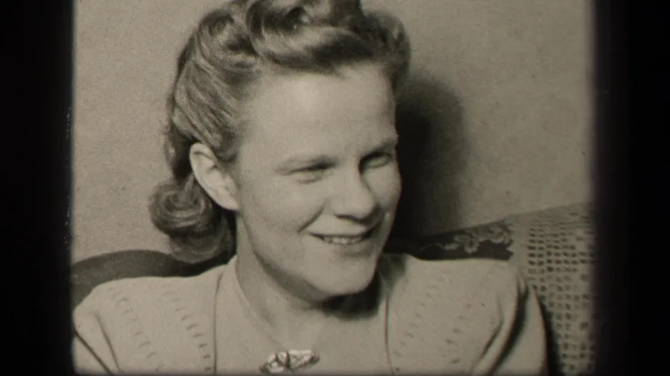 A woman in 1942 Sebring, Ohio home-movie footage smiles and looks off-camera from a seated interior position.