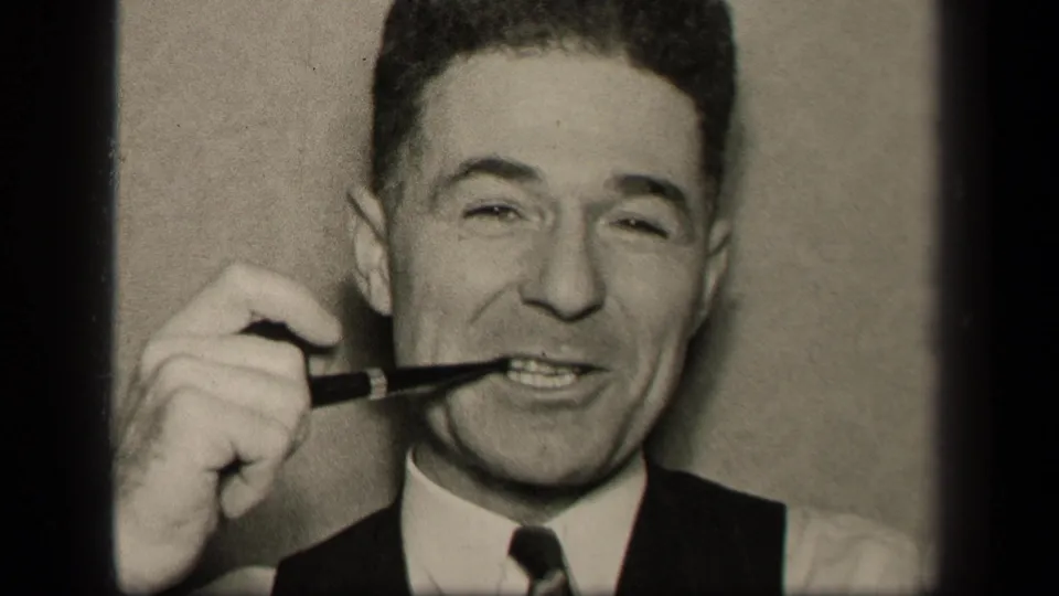 In a close 1942 Sebring, Ohio interior shot, a man smiles while placing a pipe at his mouth.
