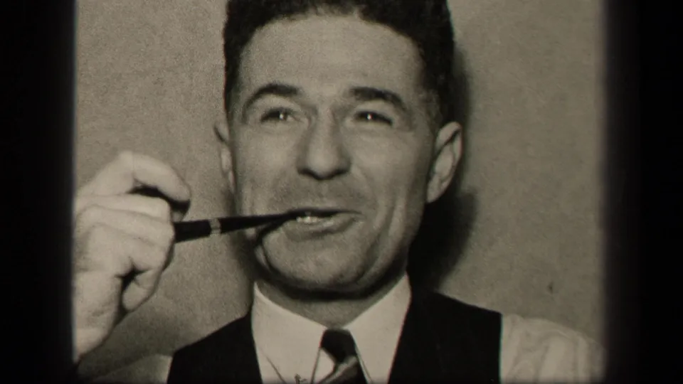 In 1942 Sebring, Ohio home-movie footage, an adult man in a vest and tie holds a pipe at his mouth and glances upward.