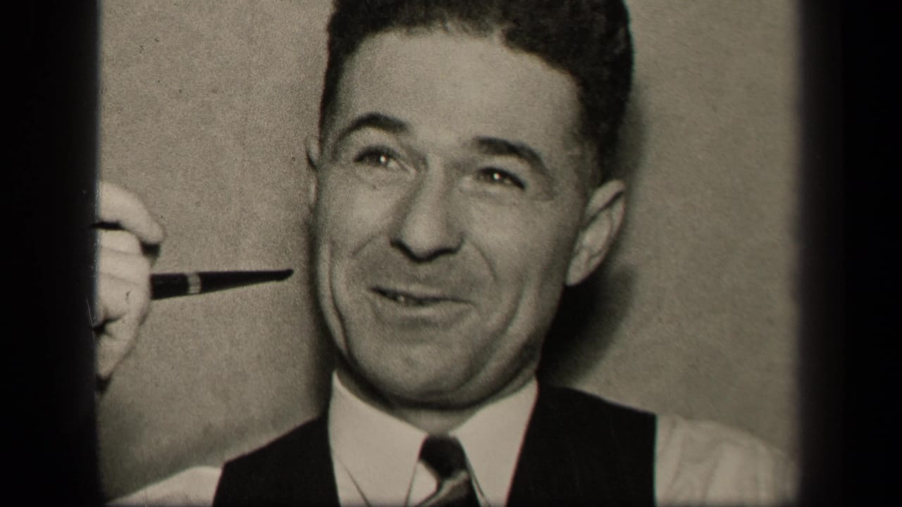 Smiling man in vest and tie holding a pipe beside his face.