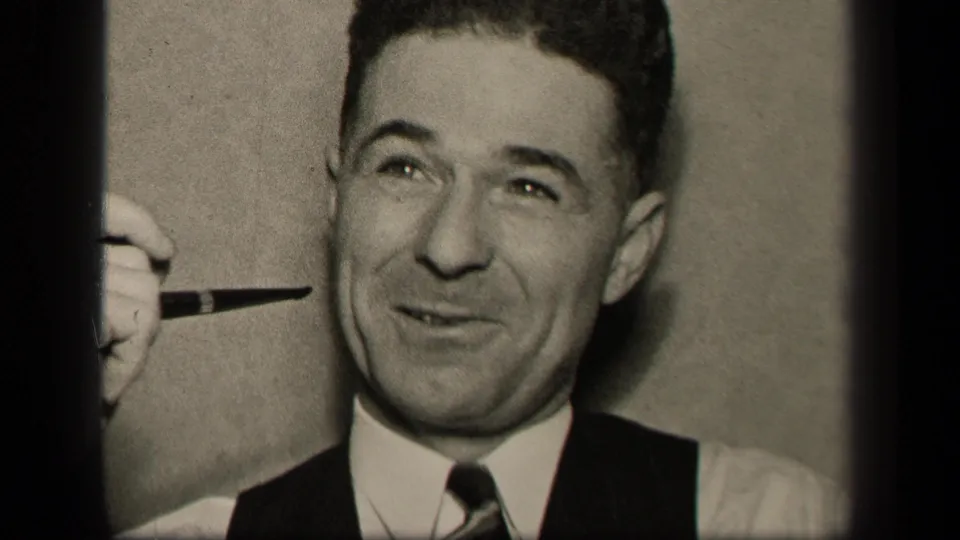 The man smiles lightly while holding a pipe near his cheek in the 1942 Sebring, Ohio 8mm home-movie frame.