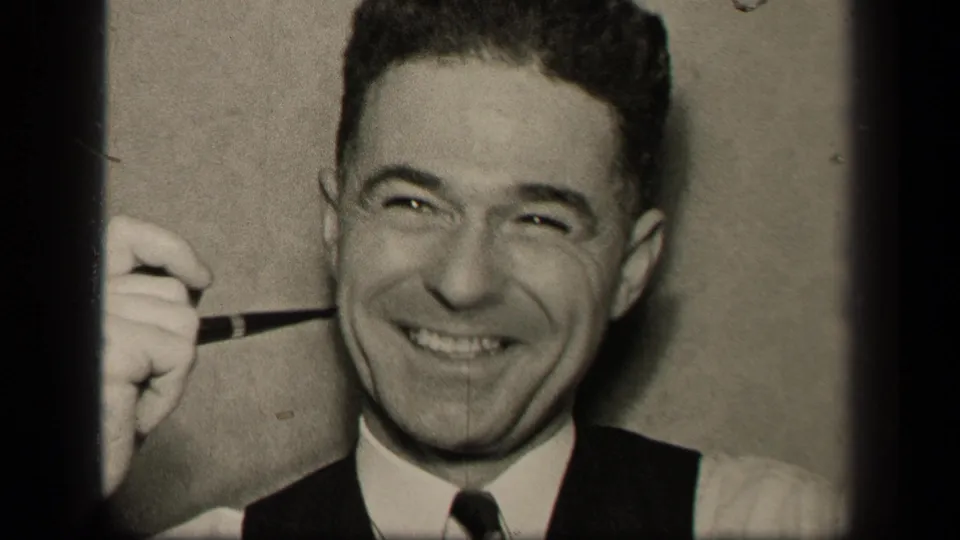 The final frame shows the adult man smiling widely, pipe lifted near his face, in grainy black-and-white 8mm footage.
