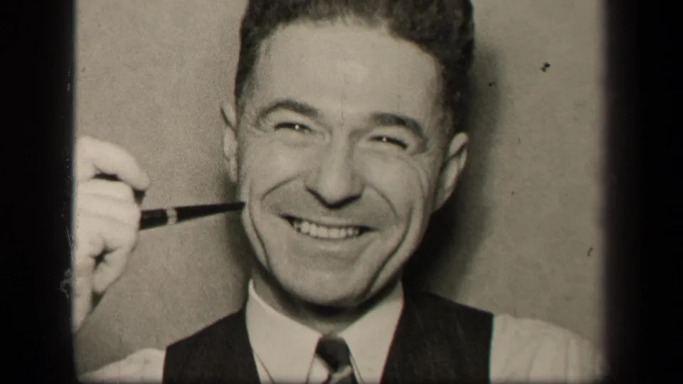 In 1942 Sebring, Ohio home-movie footage, a smiling adult man in a white shirt, tie, and dark vest holds a pipe near his cheek.