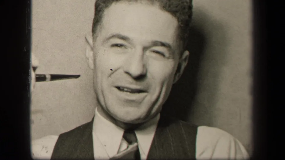 In this 1942 home-movie frame, the man appears to be speaking or reacting as the pipe is held near his face against a plain interior backdrop.