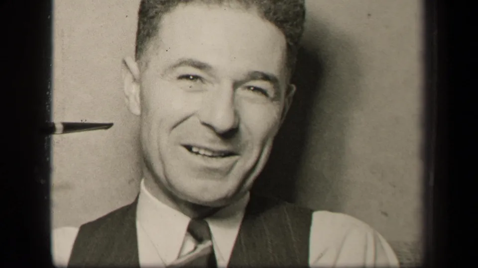 In 1942 Sebring, Ohio footage, a well-dressed adult man in a vest and tie smiles toward the camera in a domestic interior.