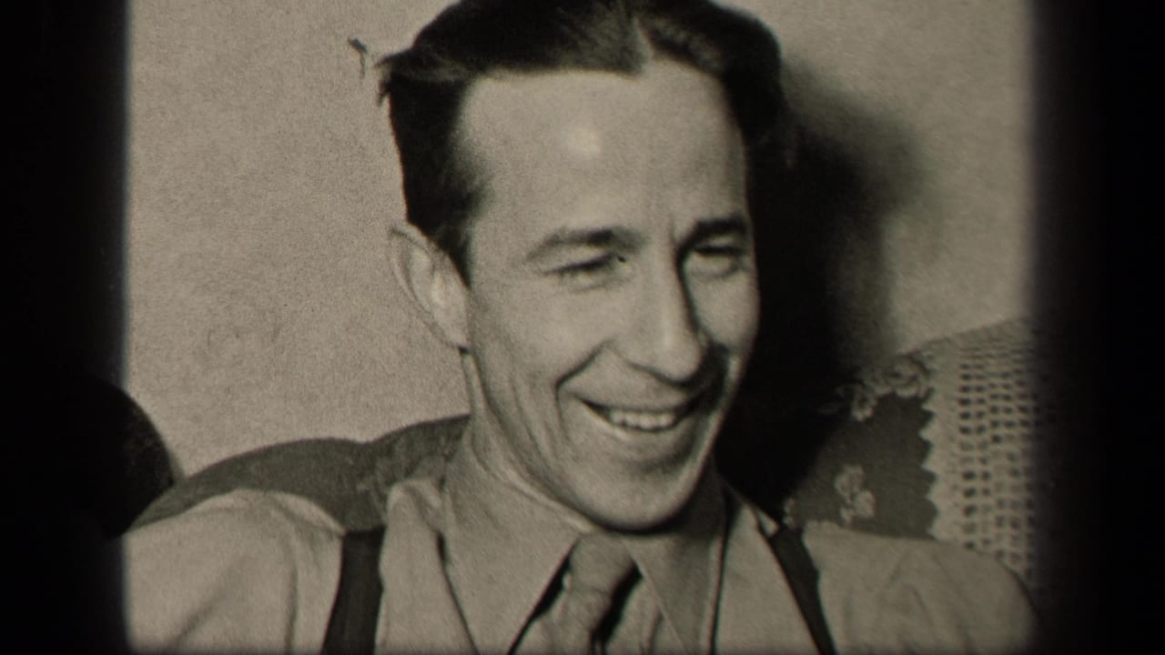 In supported 1942 Sebring, Ohio home-movie footage, an adult man smiles in close-up while seated against upholstery and a plain wall.