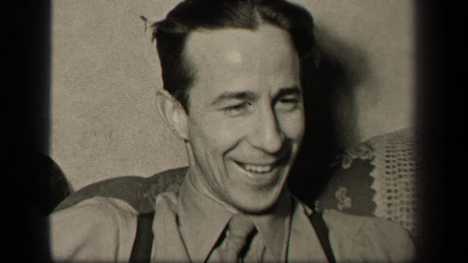 In supported 1942 Sebring, Ohio home-movie footage, an adult man smiles in close-up while seated against upholstery and a plain wall.