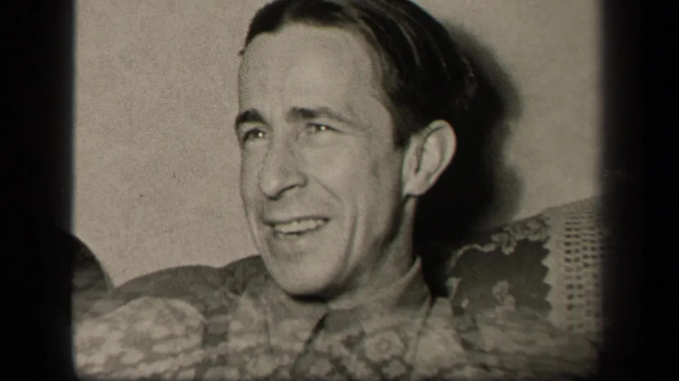 In the closing frame, the seated man looks off to the side as patterned fabric or upholstery partly enters the lower foreground.