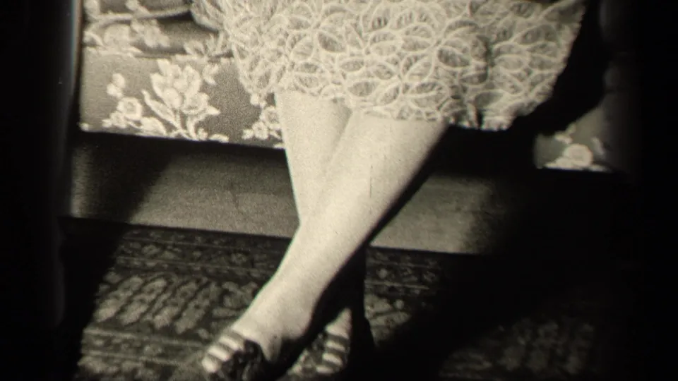 1942 Sebring, Ohio home-movie frame showing the pan upward toward a lace dress hem above crossed stockinged legs.