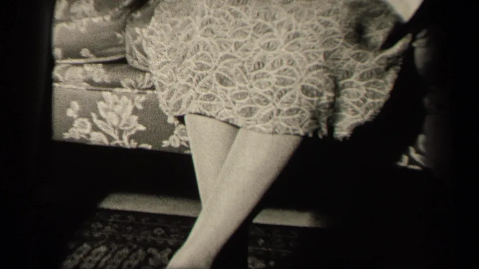 End frame from a 1942 Sebring, Ohio home movie, showing the seated woman's lace dress hem and crossed stockinged legs on a couch.