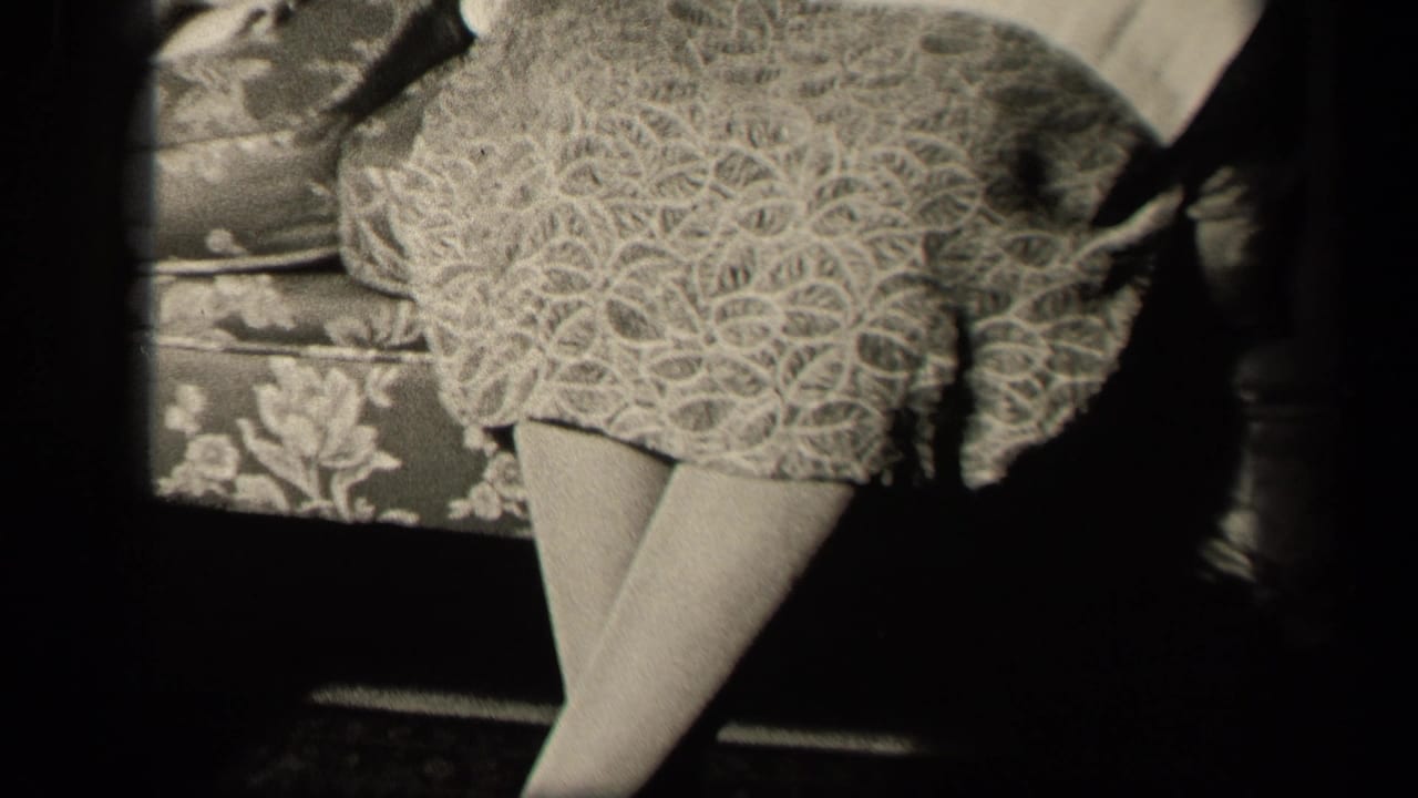 Close 1942 Sebring, Ohio home-movie frame of a seated woman’s patterned skirt, crossed legs, floral couch, and lap napkin.