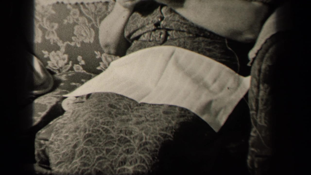In the supplied 1942 Sebring, Ohio home-movie context, a woman sits on a floral couch with knitting in her hands and a white apron across her lap.