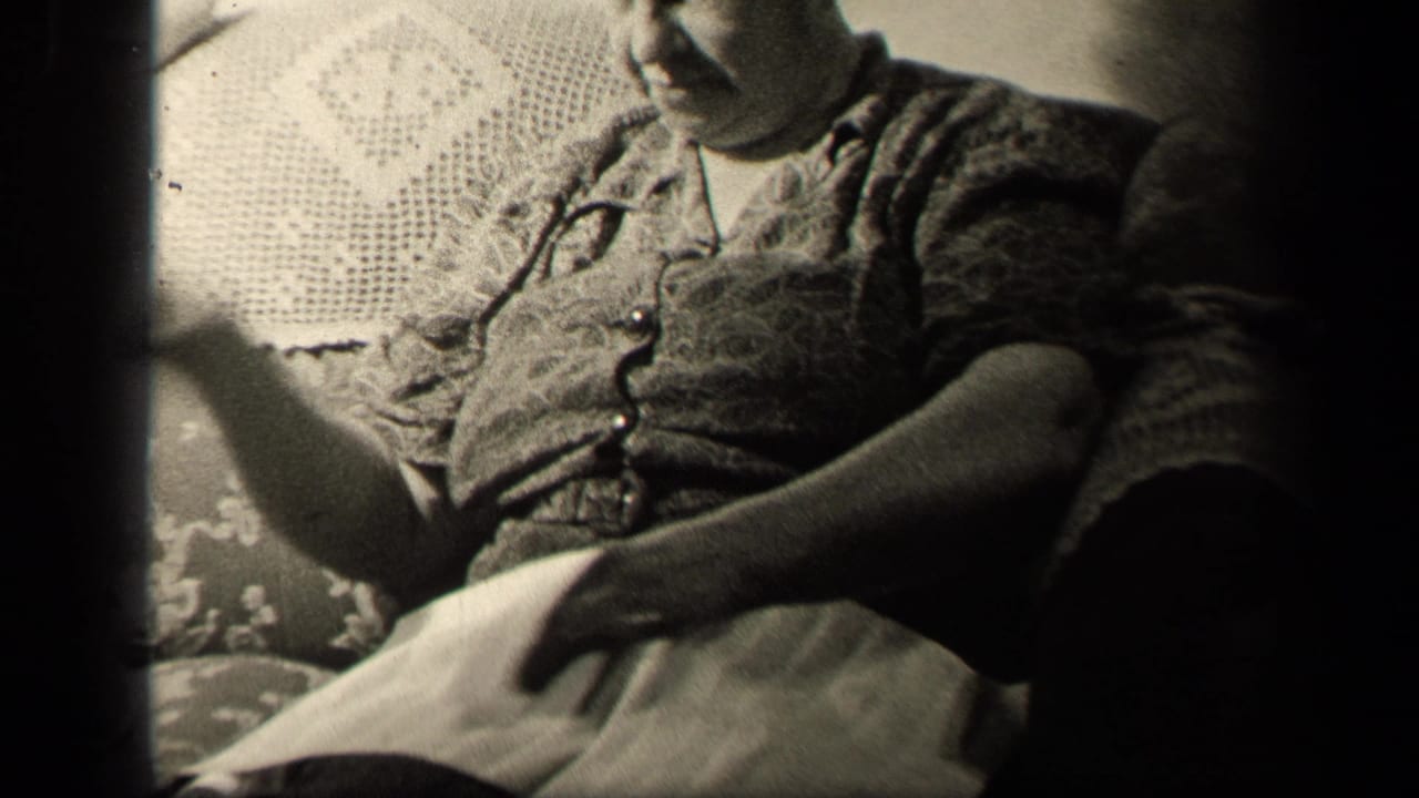 In the Sebring, Ohio home-movie frame, the woman gestures with one hand while sewing cloth rests across her lap.