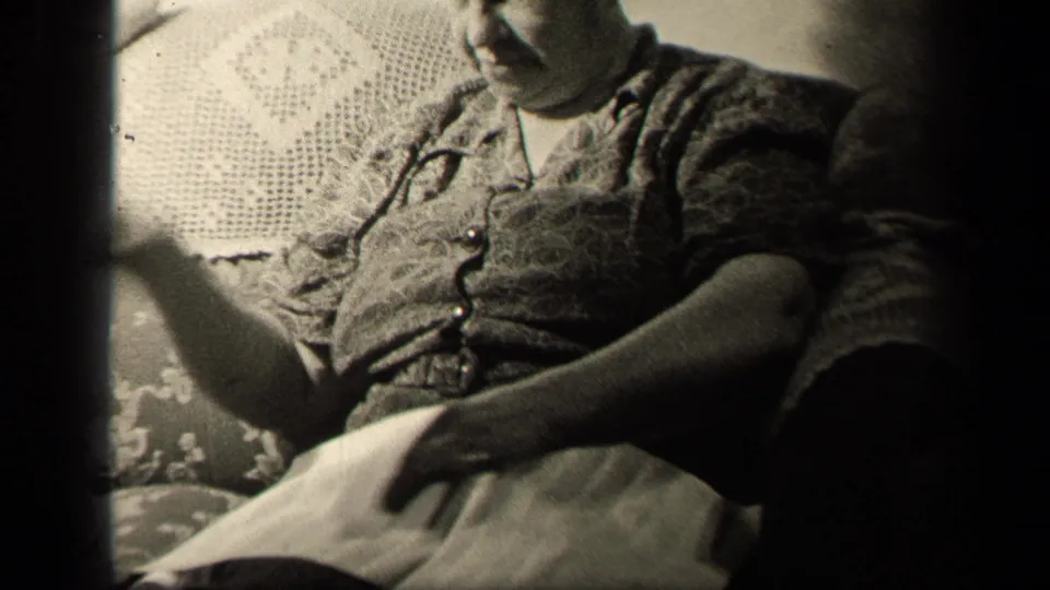 In the Sebring, Ohio home-movie frame, the woman gestures with one hand while sewing cloth rests across her lap.