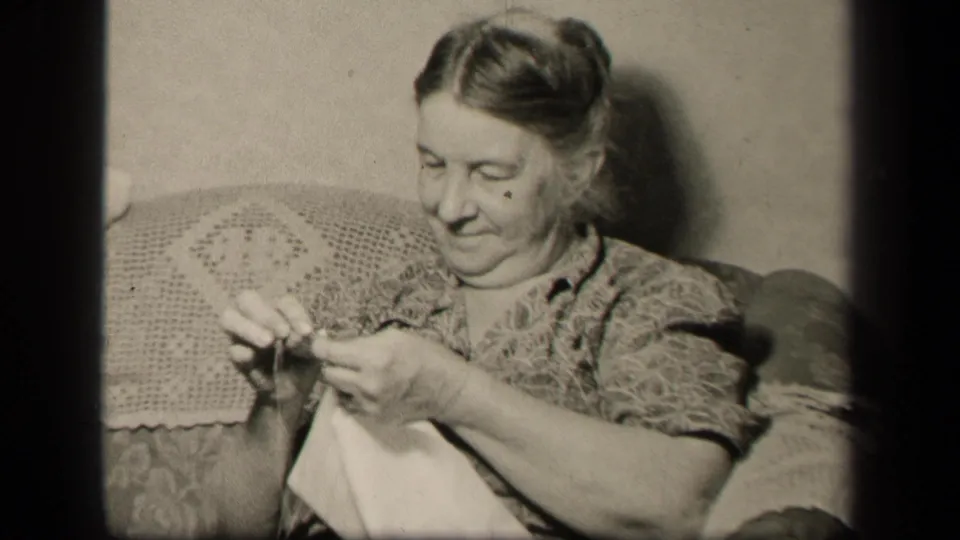 Older woman in a 1942 Sebring, Ohio living room looks down with focused hands as she threads or handles a needle.