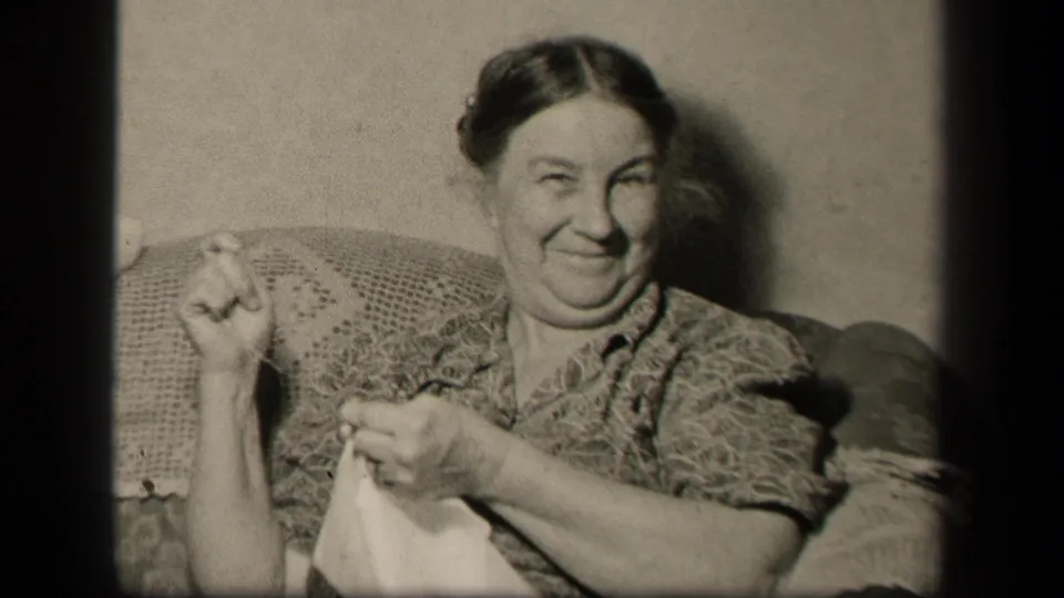 The woman smiles toward the camera with sewing in her lap, seated in a private Sebring, Ohio home interior in 1942.