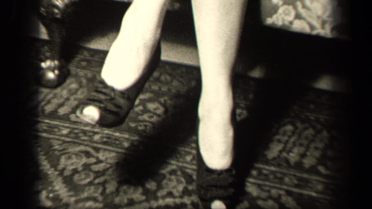 Low-angle 8mm frame from the Sebring, Ohio interior focuses on the woman's stockings and dark heels near the armchair.
