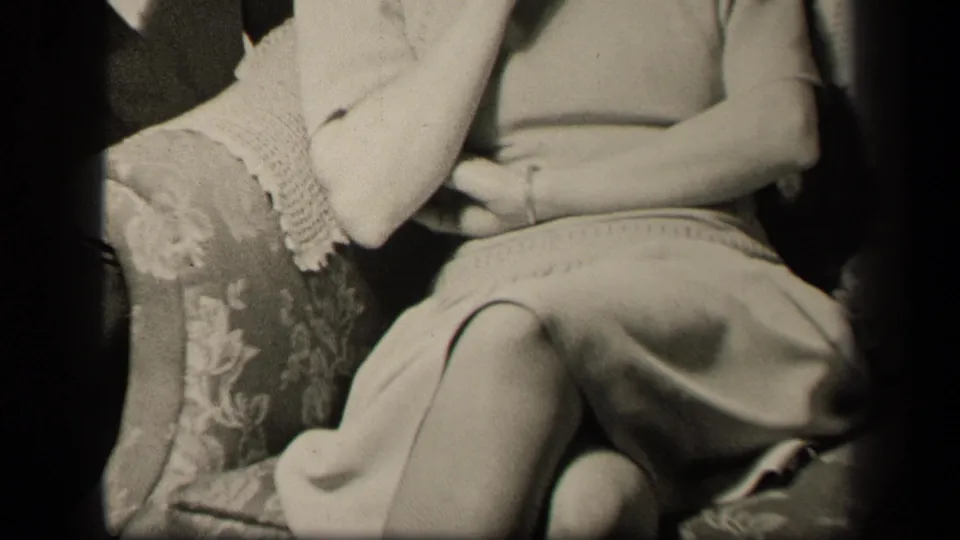 In 1942 Sebring, Ohio home-movie footage, an adult woman sits in a floral upholstered armchair with her hands folded in her lap.