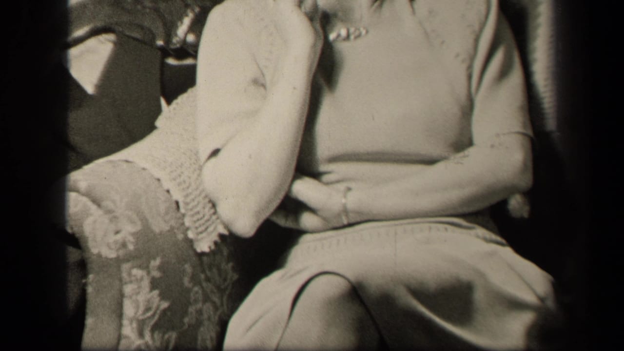 The camera continues upward on the seated woman in the ornate armchair, with her cardigan sleeve and lap still prominent.