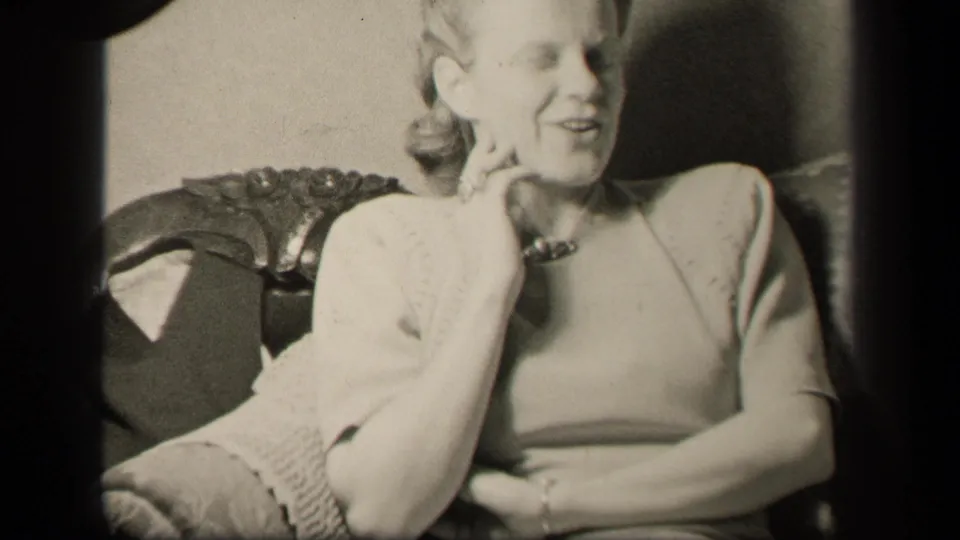 Adult woman in 1942 Sebring, Ohio home-movie footage smiles in an ornate chair with her hand near her face.