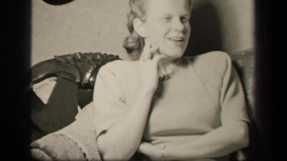 Woman in 1940s dress sits in an ornate chair in Sebring, Ohio, smiling with her hand raised near her cheek.