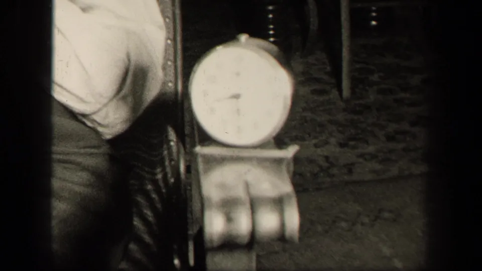 In 1942 Sebring, Ohio home-movie footage, a round analog clock sits on a small table near the woman's chair in a private interior.