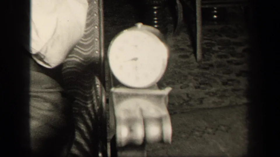 In 1942 Sebring, Ohio home-movie footage, the camera holds on a round analog clock on a table near an ornate chair and patterned floor covering.