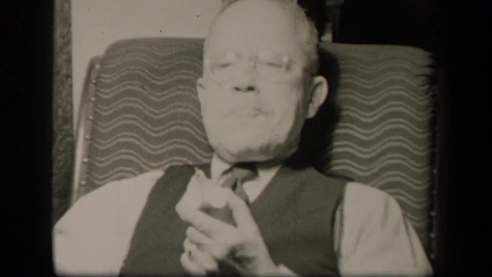 Older gentleman in a vest and tie sits back in the patterned chair after biting fruit, filmed inside a private Sebring home.