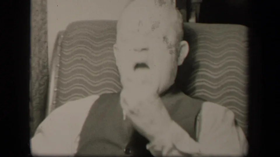 The seated elderly man in Sebring, Ohio appears to bring his hand to his mouth while framed closely against the patterned chair.