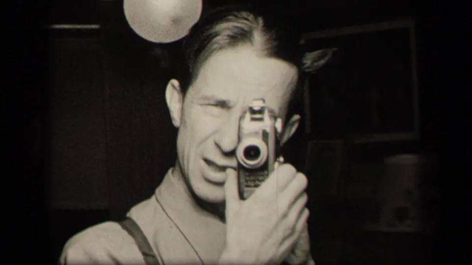 In a 1942 Sebring, Ohio home-movie frame, a man films his reflection with a compact camera beneath a globe lamp.