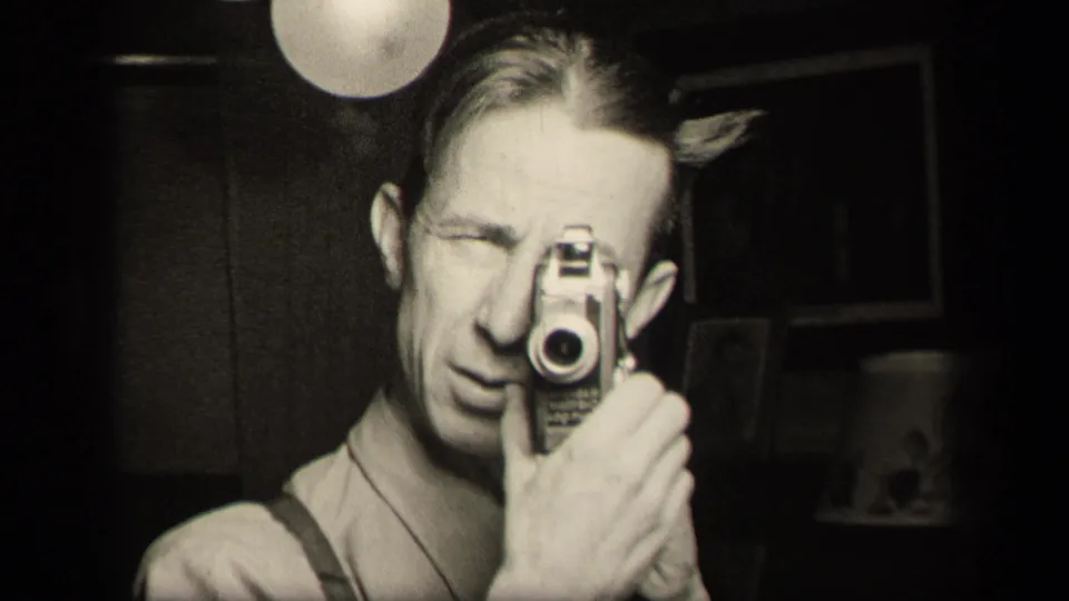 A grainy black-and-white frame shows the man filming himself in a private Sebring interior with a globe lamp overhead.