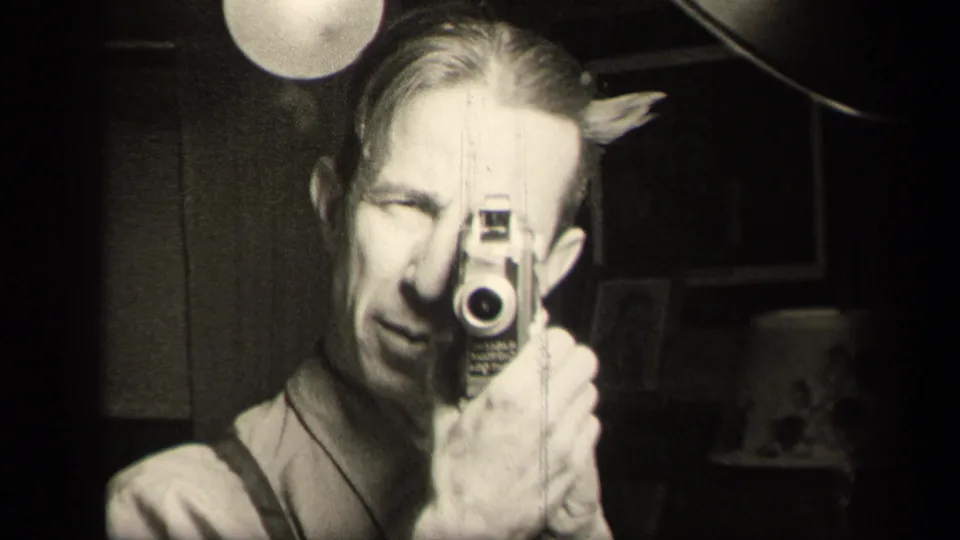In Sebring, Ohio 1942 home-movie footage, a man in suspenders peers through a small camera in a dark interior.