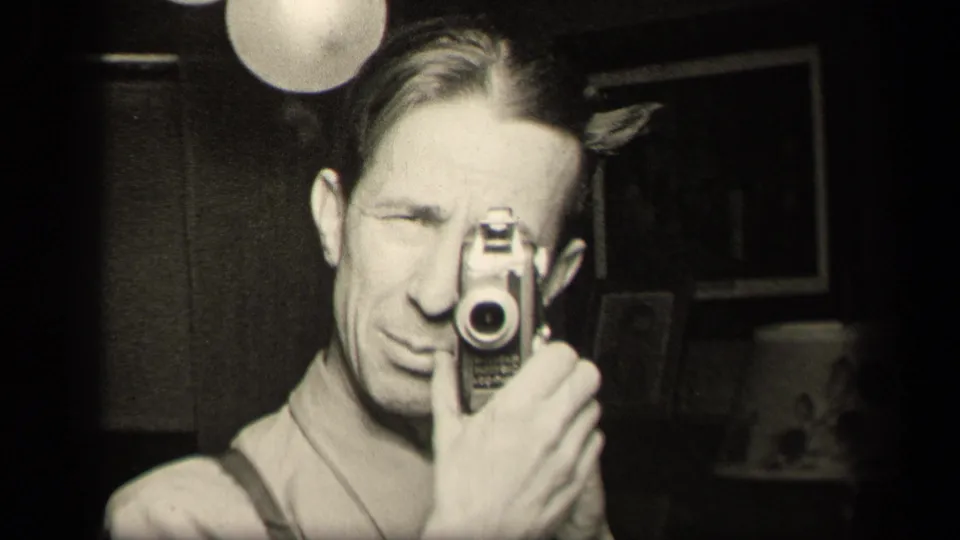 A 1942 Sebring, Ohio home-movie frame shows a man holding a small camera to his eye in a dim private room.