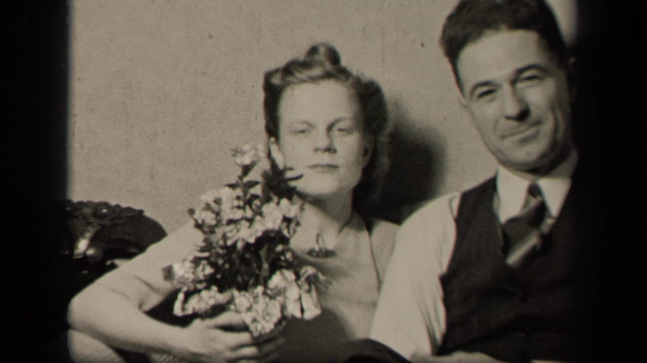 Bride holding a bouquet sits beside a smiling groom in black-and-white home-movie footage.