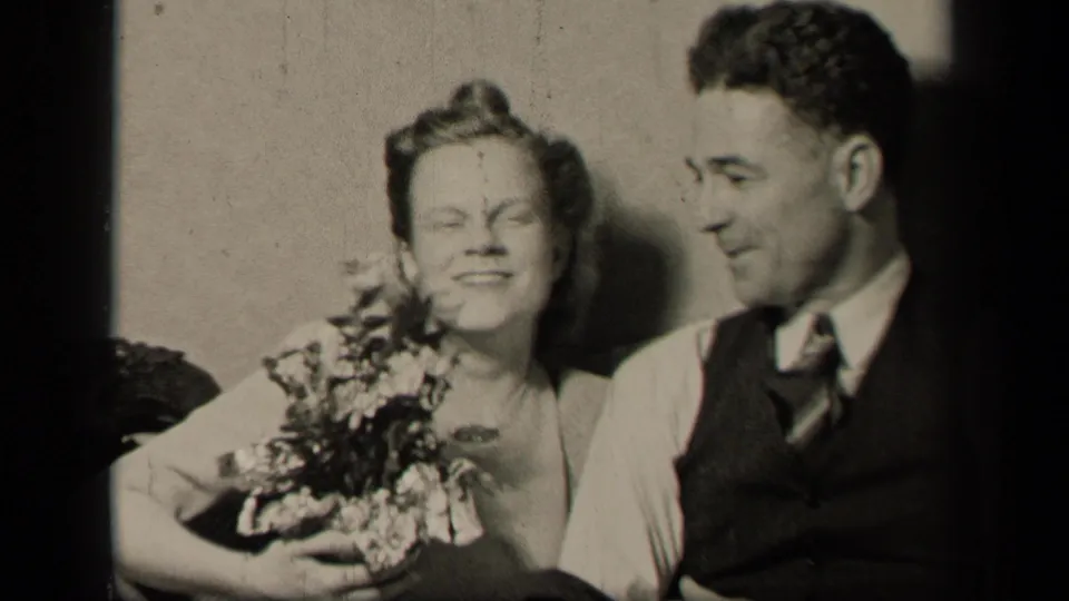 1942 Sebring, Ohio frame of the bride smiling with flowers as the groom looks toward her in a close seated portrait.