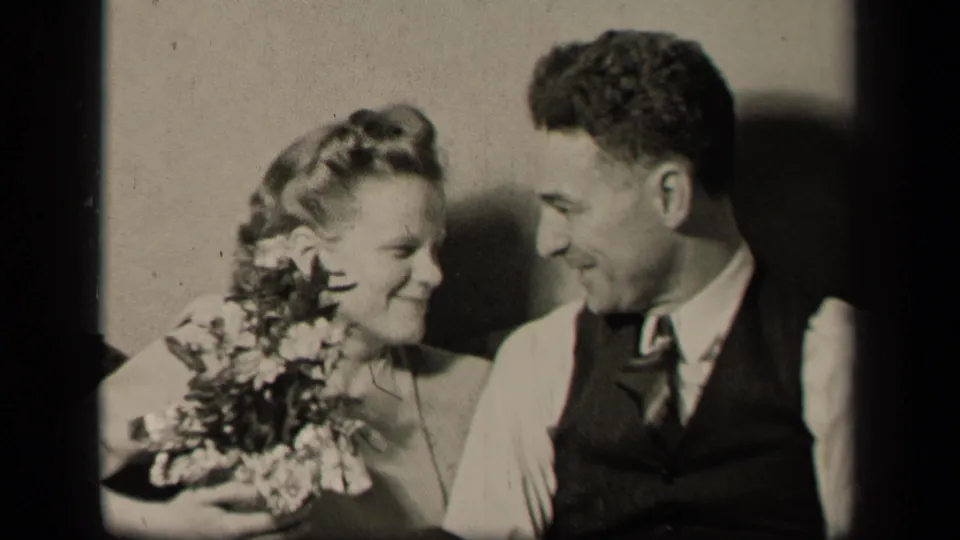 1942 Sebring, Ohio home-movie frame showing the newlyweds sharing a close smile beside the bride's bouquet.