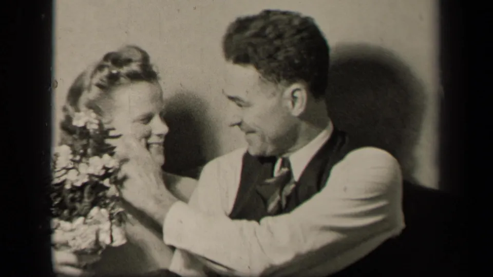 1942 Sebring, Ohio frame with the groom gently touching the bride's face while she smiles beside her bouquet.