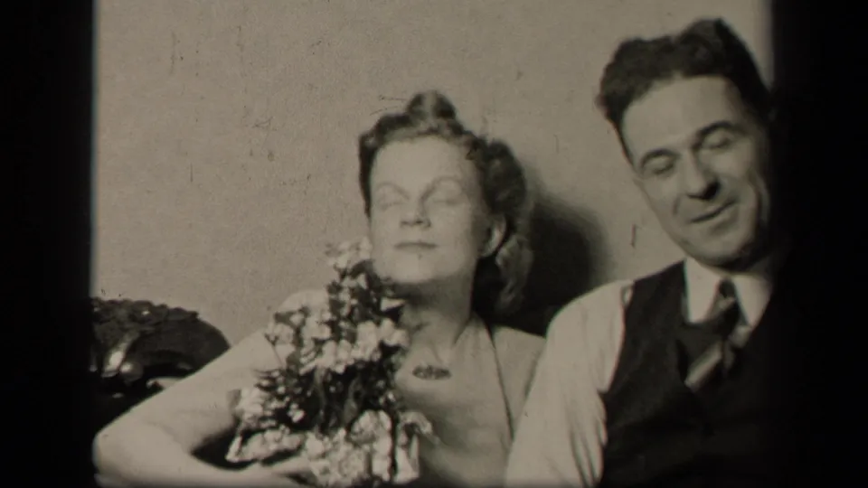 In the final frame, the woman with flowers and the man in formal dress sit close together against a plain wall.