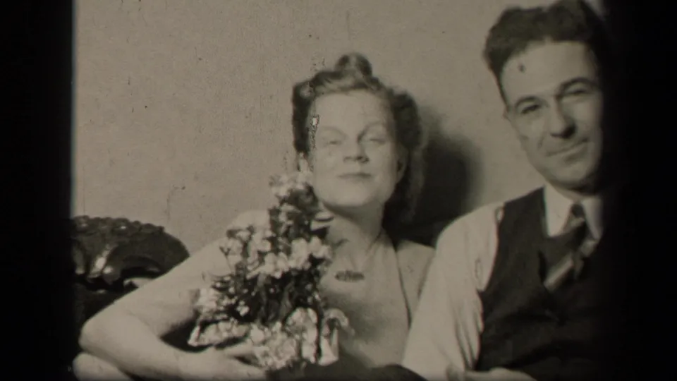 In metadata-supported Sebring, Ohio, 1942, a woman with flowers sits close to a man in a vest and tie on a sofa.