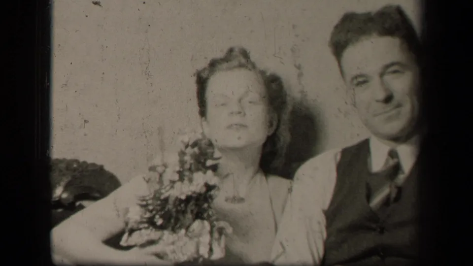In this 1942 Sebring, Ohio home-movie frame, the woman lifts her face while holding flowers and the man sits close beside her.